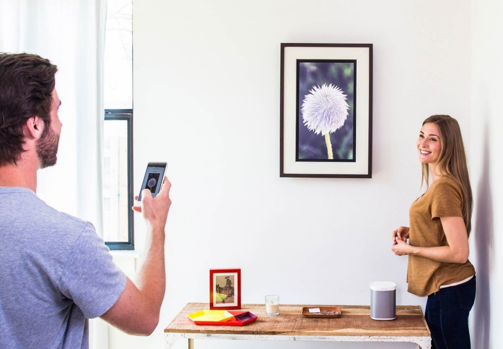 A man uses art streaming platform, Acanvas, to connect his phone to one of its cord-free customizable digital frames, while a woman oversees with a smile on her face