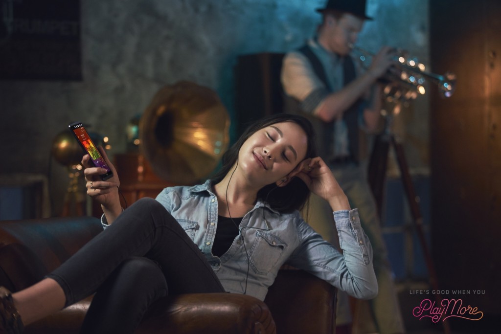 A woman relaxing in a chair and listening to music with Spatial Audio via smartphone with headphones on