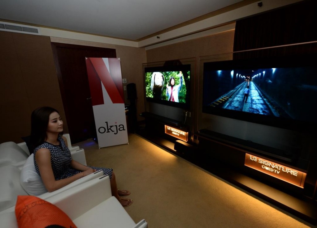 A female model watches Okja on LG’s 2017 SIGNATURE OLED TV W, Netflix promotional standing banner visible at side of room