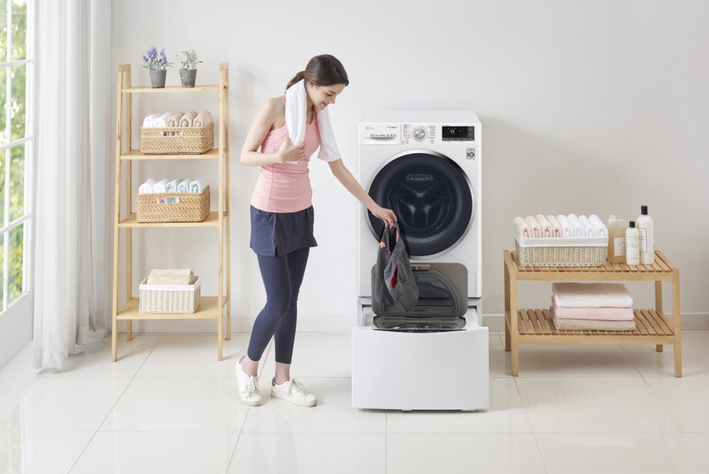 A woman in athletic wear putting gym shorts in the LG TWINWash™ Mini unit of the TWINWash™ washing machine in a laundry room