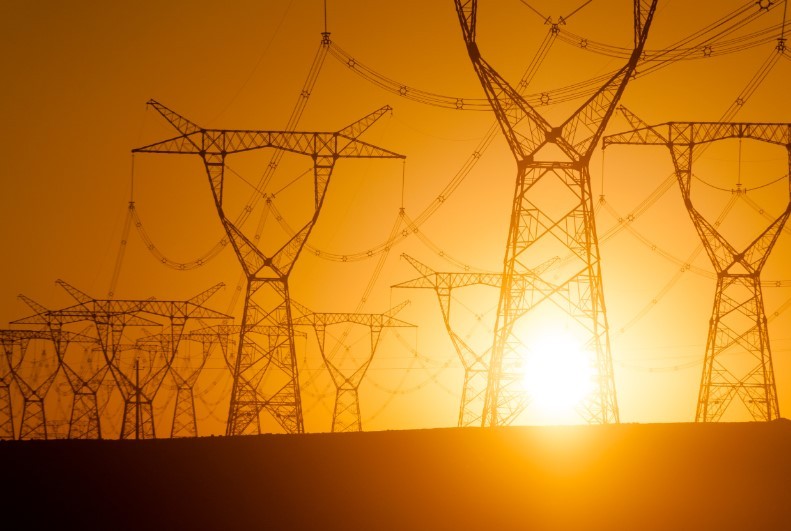 Huge metal power poles and thick wires that transfer the high-voltage electricity in front of the sunset glow