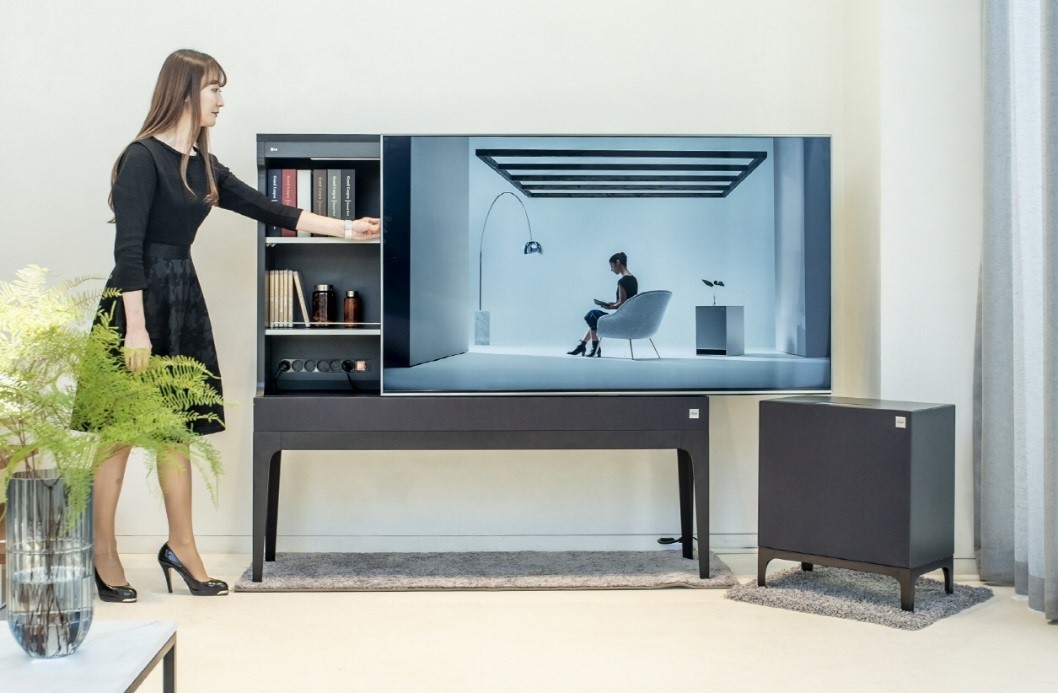 A woman slides open the display panel of LG Objet TV in order to use the storage hidden behind the panel