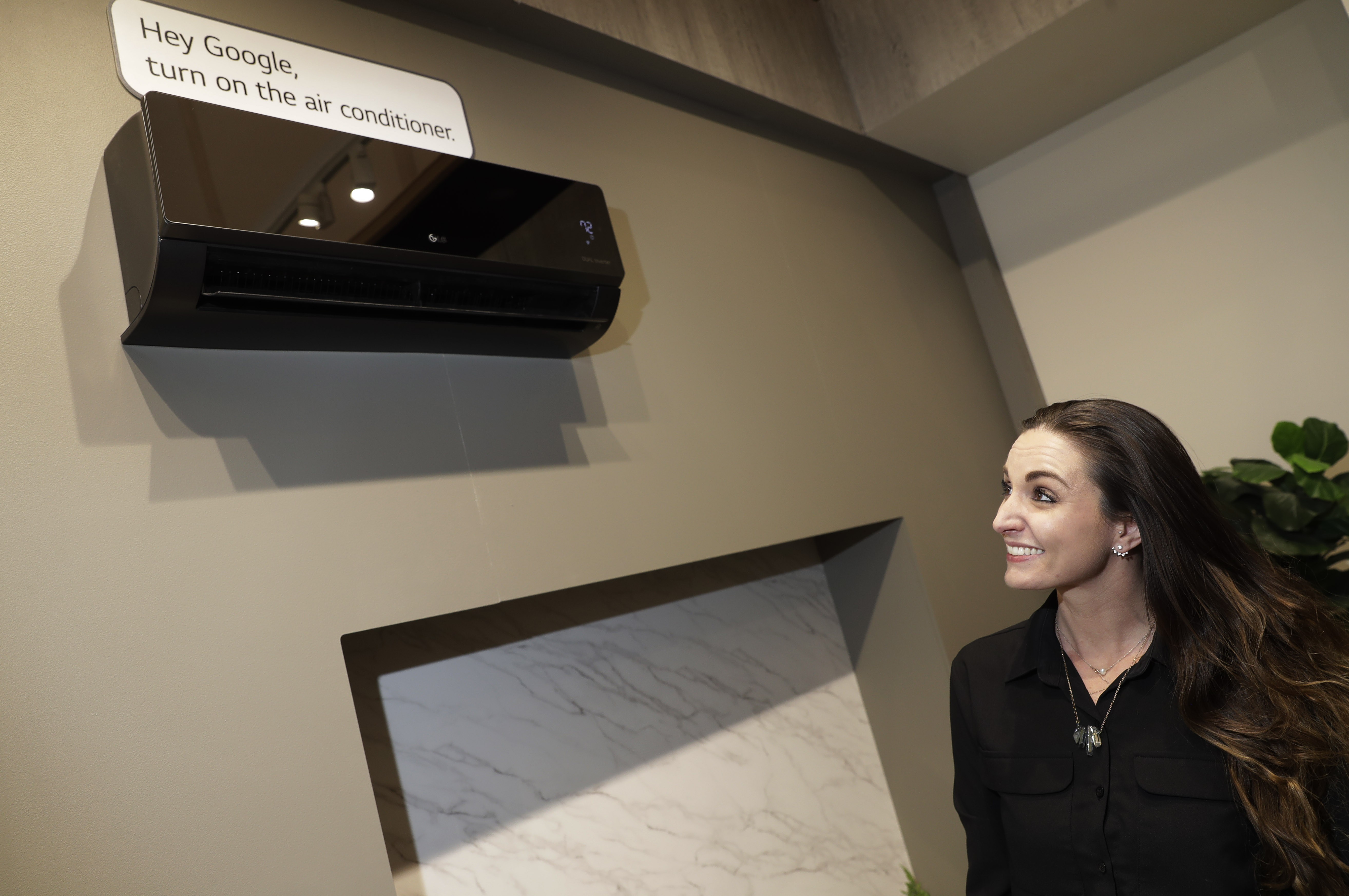 Woman looking up at a black LG air conditioner with a sign that says “Hey Google, turn on the air conditioner”