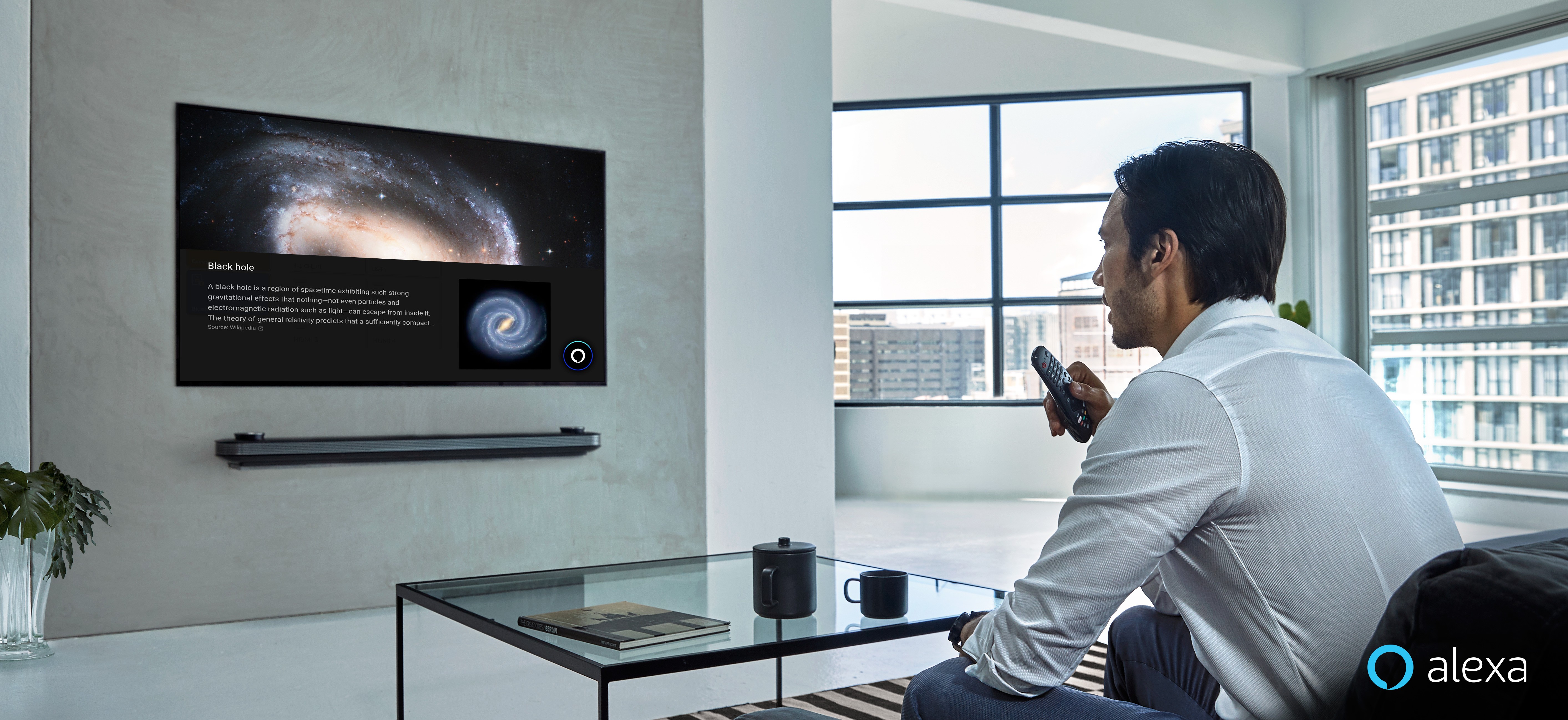 A man is watching LG TV supporting Amazon Alexa while holding the remote in one hand at home.