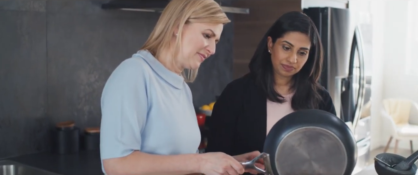 Two ladies behold ingredients while pouring them down from a pen.