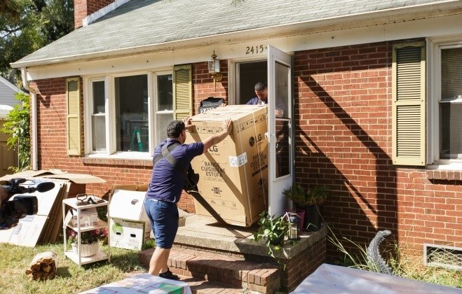 Two volunteers bring LG-donated home appliance into a house of Charlotte’s Druid Hills neighborhood.