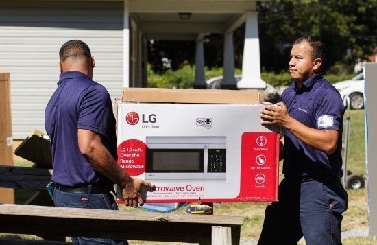 Two volunteers carry LG’s microwave oven to bring it into a house of Charlotte’s Druid Hills neighborhood.