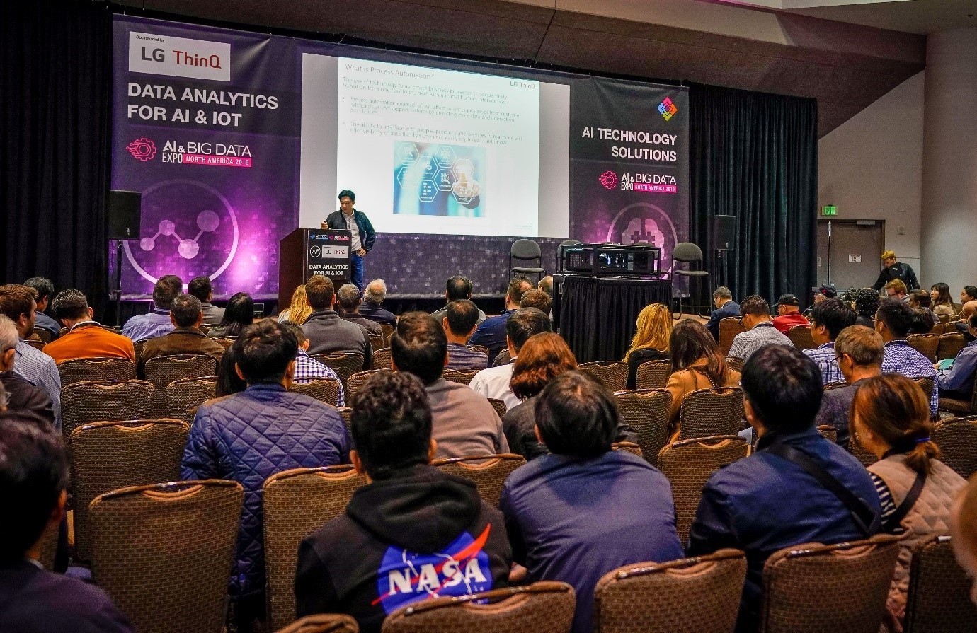 Samuel Chang, corporate vice president of the LG Silicon Valley Lab, discusses Process Automation from IoT Data in front of a large audience, with a large banner bearing the LG ThinQ logo behind him.