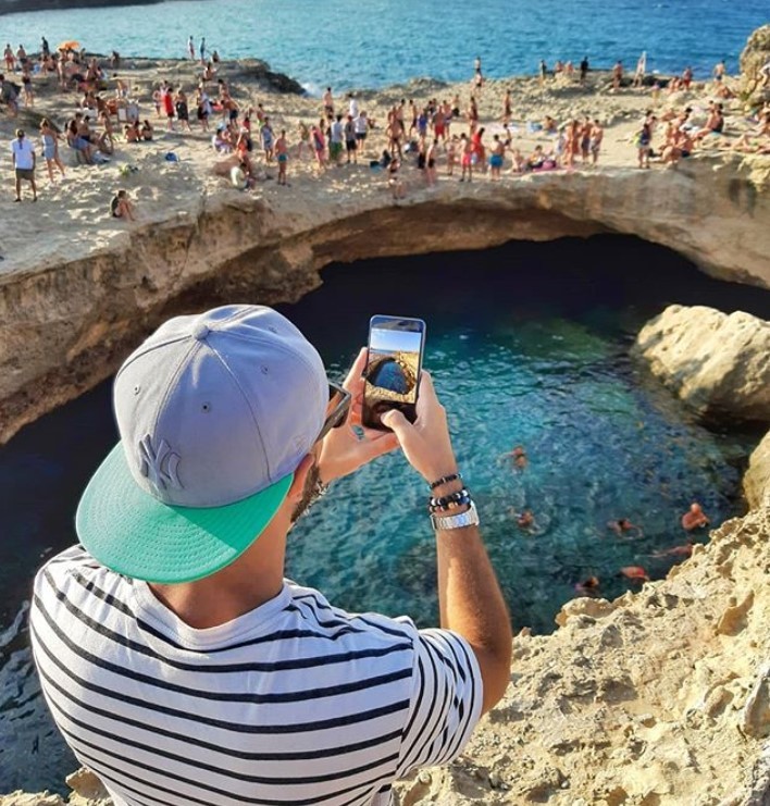 A male Instagram influencer shoots a video of the coast with his LG smartphone while people enjoy the beautiful weather.