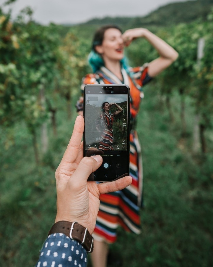 A man holding up an LG smartphone to take a photo of a woman posing as she eats grapes.