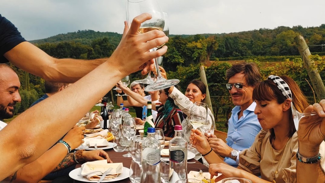 An image of friends enjoying lunch outdoors with beautiful green trees and hills in the background.