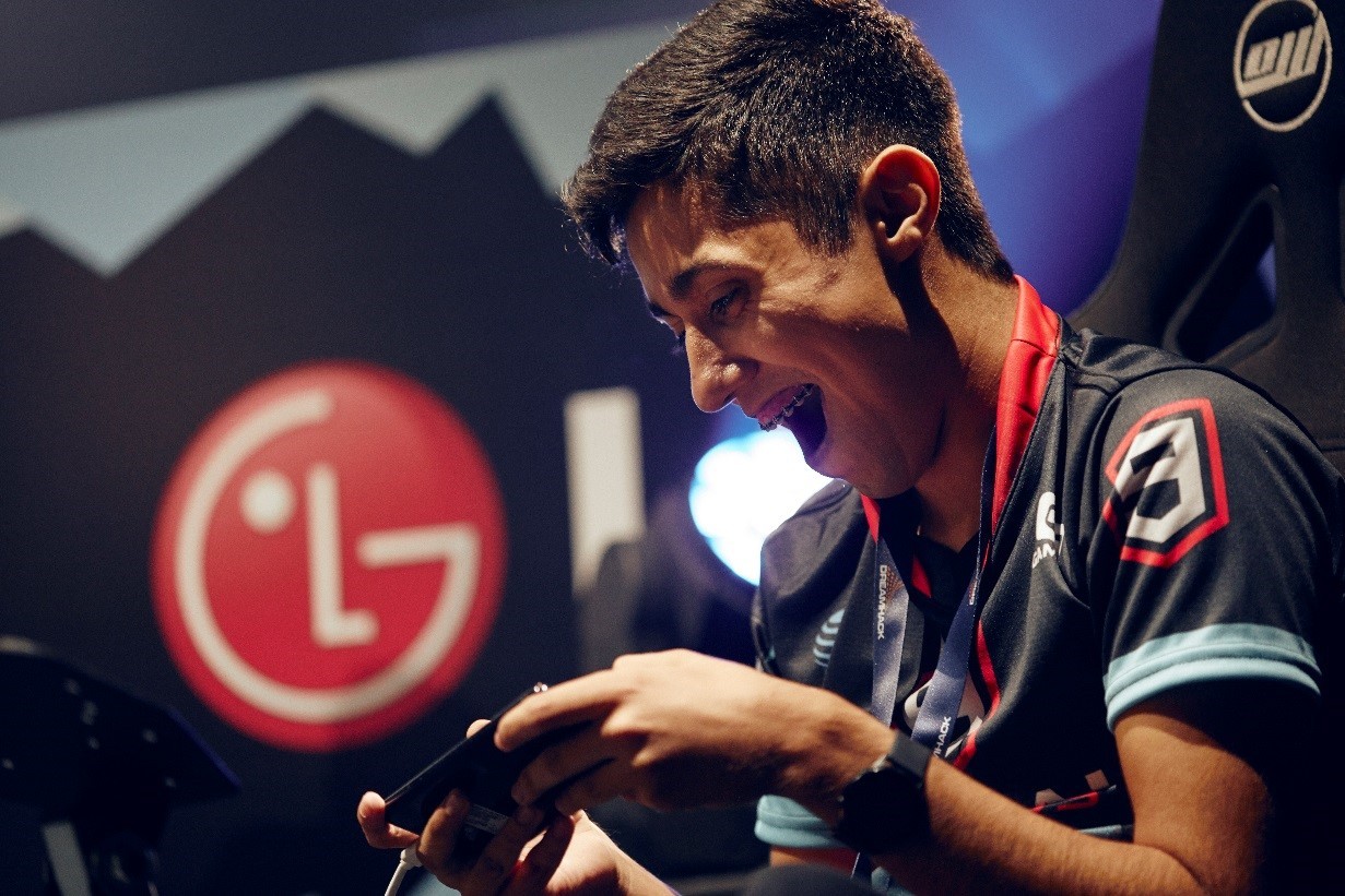 A male gamer plays a video game on the LG G8X ThinQ with Dual Screen, with a large LG logo on the wall in the background.