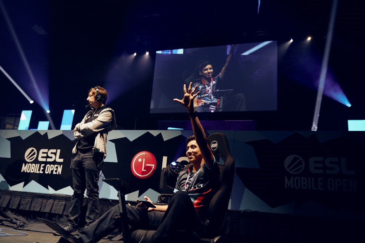 A gamer waves to spectators as he sits on a gaming chair center stage.