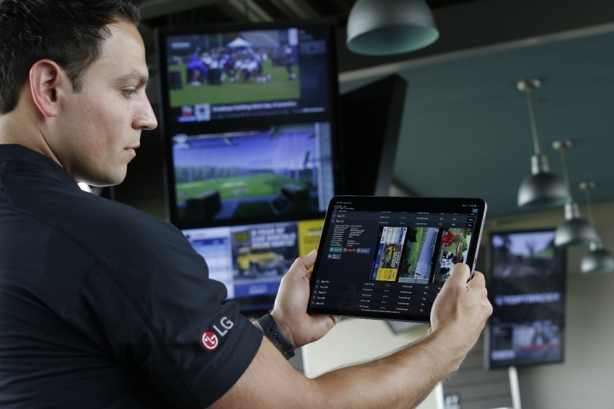 Another image in which a man holds up a SAVI Canvas tablet to remotely manage the information displayed on LG’s commercial digital signage solutions.