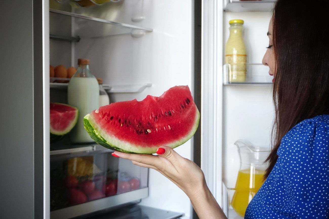 A woman takes a few bites of a slice of watermelon she just took out of the LG refrigerator.