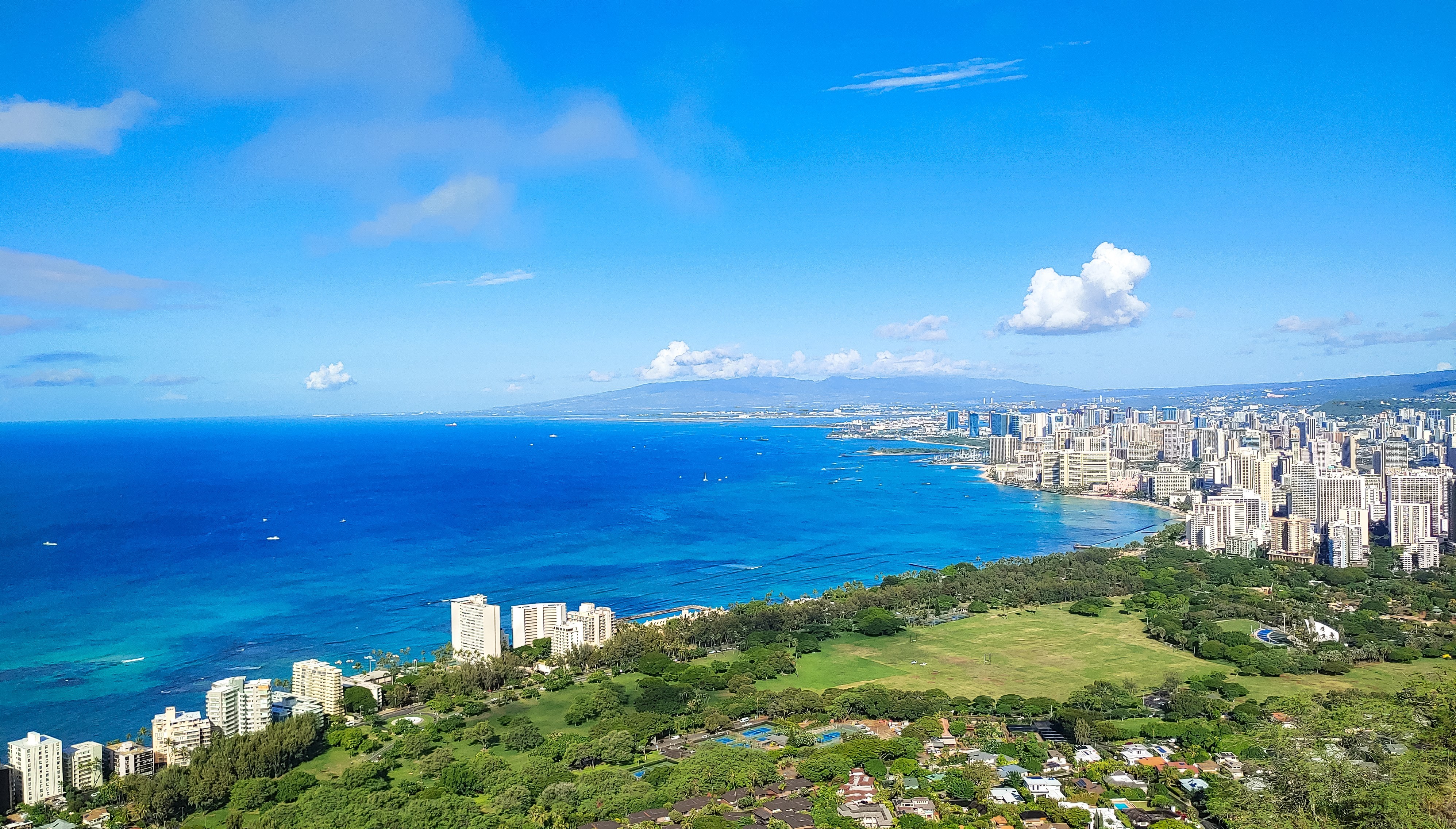 A wide-angle landscape photo taken by LG G8X ThinQ captures the beautiful blue sea and green hills of a town by the beach in Honolulu, Hawaii on a sunny day.