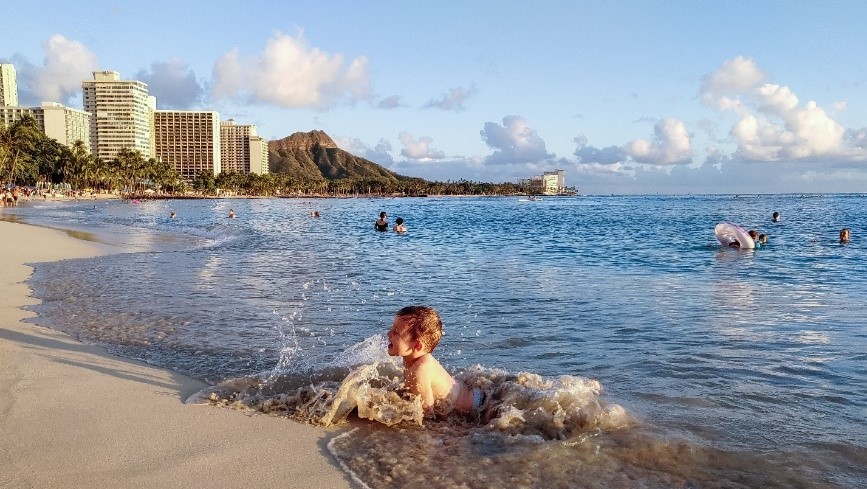 A photo taken by LG G8X ThinQ captures the special moment of a child splashing in the waves on the shore of a Hawaiian beach.