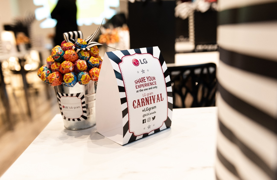 A sign for the LG gram Carnival stands on a table next to an LG-branded pot filled with lollipops