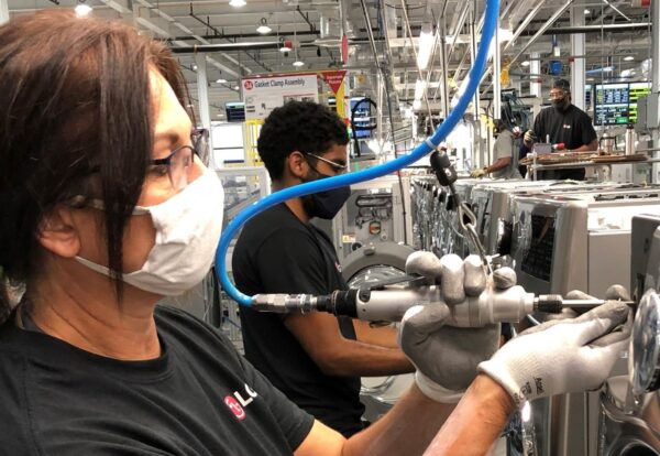 One LG factory worker using special equipment to assemble the washing machine’s front panel while others work in the background