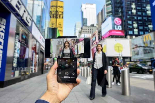 A person taking a picture of a woman walking toward the camera in Times Square with the help of LG WING's Swivel Mode capabilities