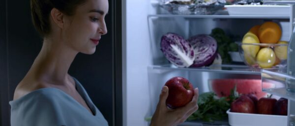 A woman takes an apple from her fruit and vegetable-filled LG refrigerator that keeps ingredients fresher for longer with HygieneFRESH+™ and LINEARCooling™ technology