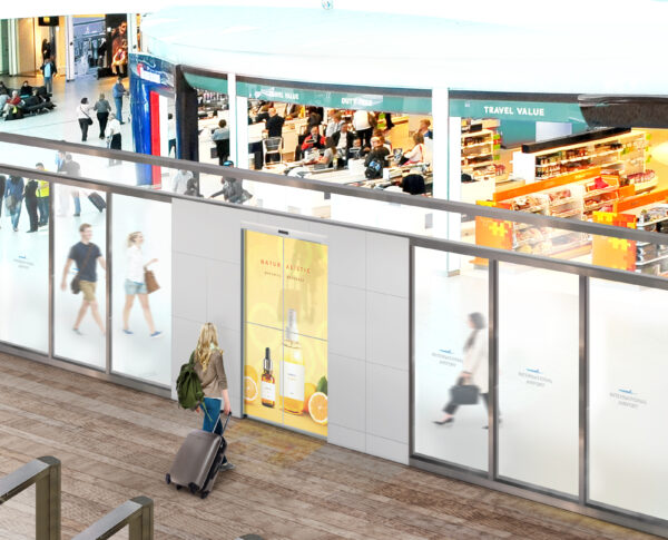 A woman entering the departures terminal of an airport through a transparent OLED automatic door which is displaying a product advertisement