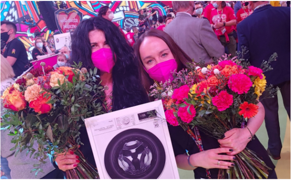Two female fundraisers holding flowers and a picture of the donated LG Vivace washer dryer in the studio.