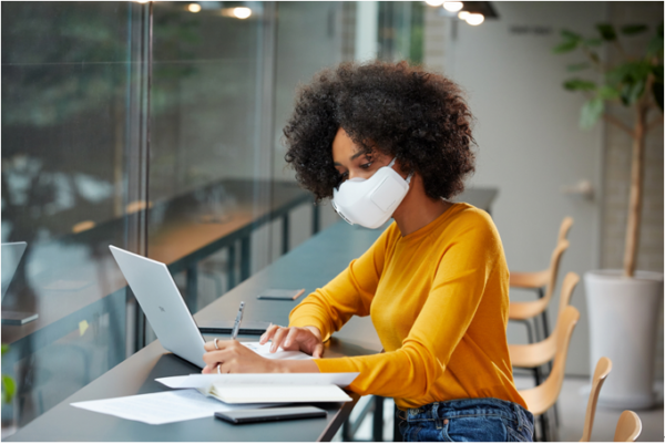 A woman wearing LG PuriCare™ Wearable Air Purifier as she works on a laptop at a cafe to protect herself during uncertain times.