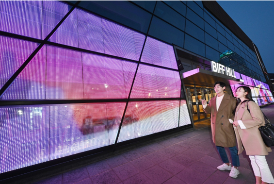 Busan Sinema Merkezi'nin cephesinde sergilenen LG Şeffaf LED Filmine hayran olan bir erkek ve bir kadın.
