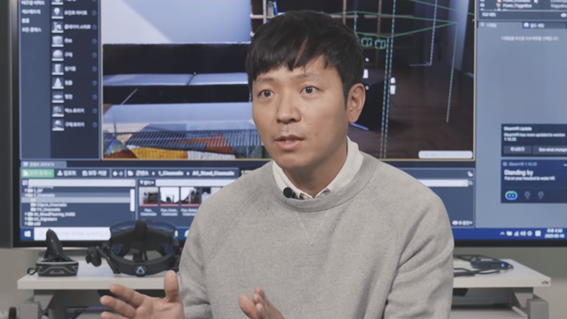 Ryu Byeong-gi, another featured digital designer at LG, explaining the role of a digital designer in front of his workspace equipped with a VR headset and large TV.