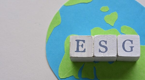 Three cubes displaying letters from the acronym ESG stand on top of a handmade picture of the world.