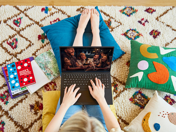 A woman sitting comfortably on the floor with colorful cushions as she watches a TV show on her LG gram.