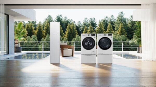 The white LG Styler and LG TWINWash being displayed in a spacious living room that overlooks a pool and a green forest.