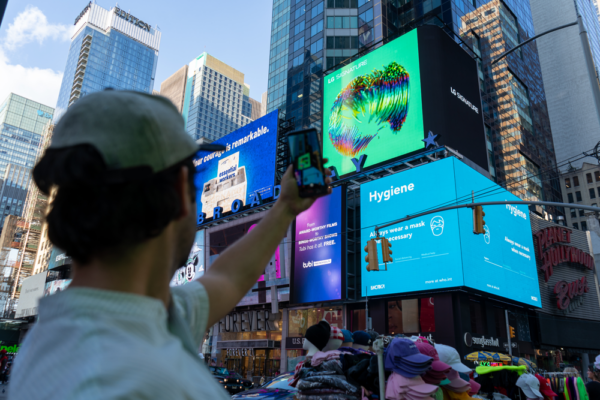 A man taking a picture of LG's massive, high-definition digital billboard in Time Square, New York displaying the artwork of David McLeod