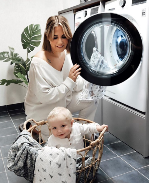  A woman using an LG washing machine to do her laundry as her baby plays inside the clothes basket.