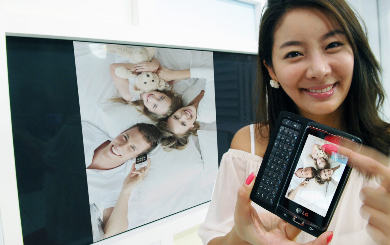 A female model is showing a family photograph on the TV by using LG’s unique multimedia sharing technology on her LG Optimus 7