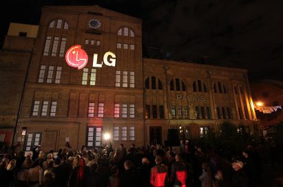 A large audience observes a gigantic 3D LG logo projected onto the front of a building in Kulturbrauerei, Berlin