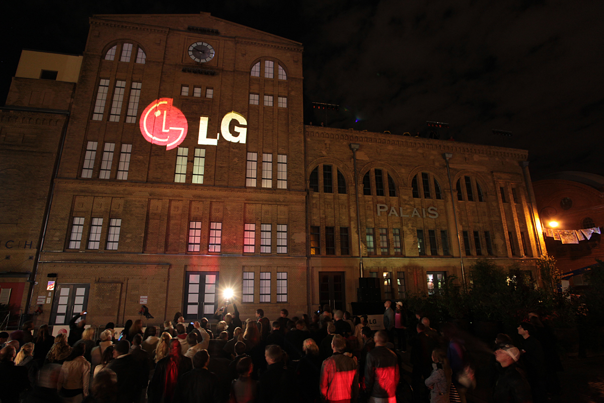 A large audience observes a gigantic 3D LG logo projected onto the front of a building in Kulturbrauerei, Berlin.