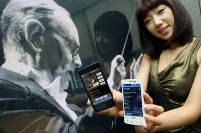 A female model holds black and white LG Optimus 2Xs in front of a photo of movie soundtrack maestro, Ennio Morricone