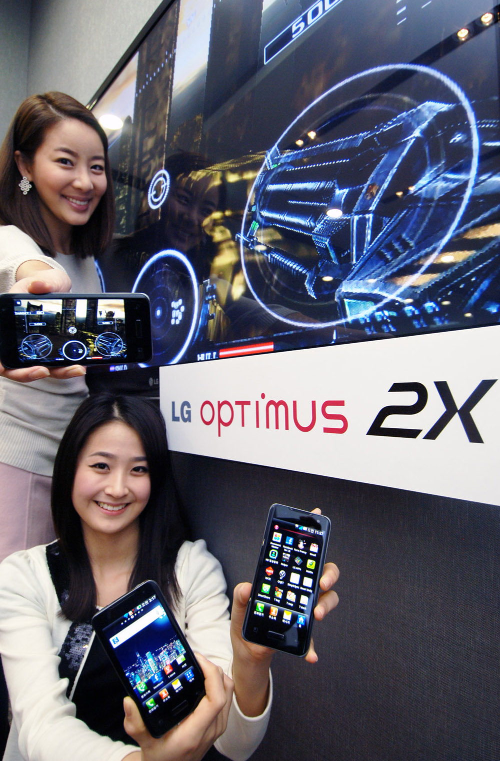 Two models pose with three LG Optimus 2X smartphones next to an LG TV showcasing the phone’s gaming potential.