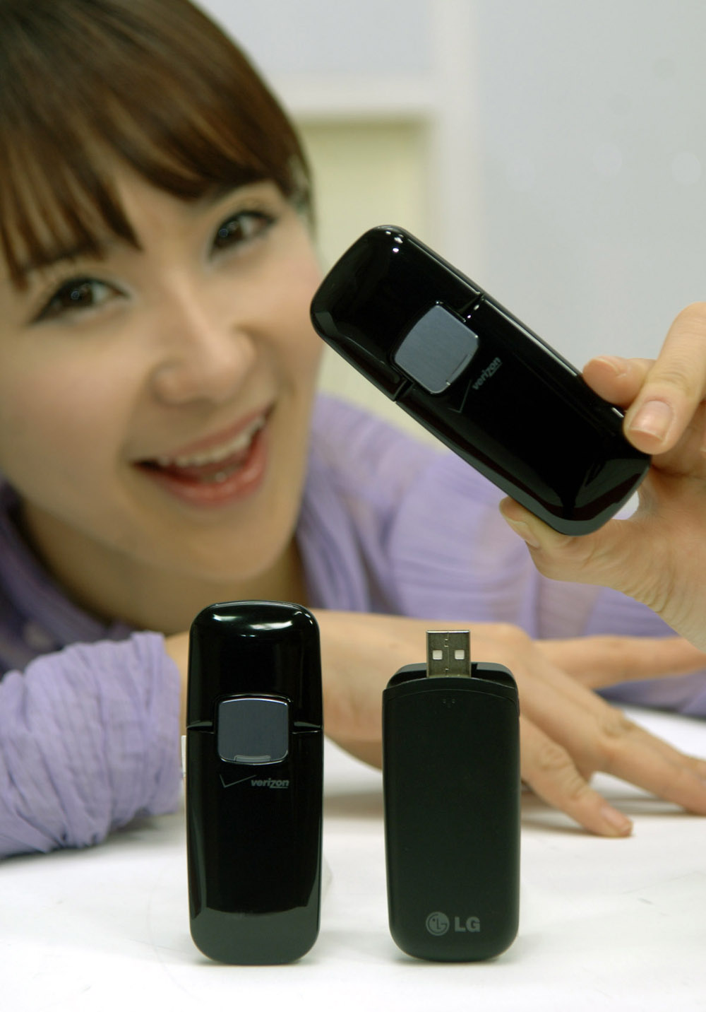 A model posing with a closed LG Verizon Wireless LTE USB Modem while two stand up perfectly on the table, one with the lid open and the other with the lid closed