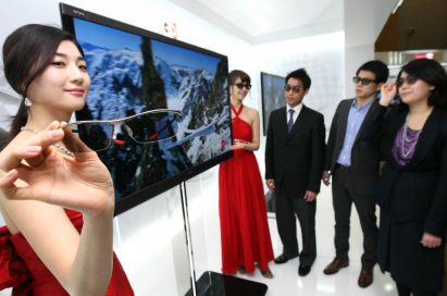 Another view of LG’s NEW CINEMA 3D TV with models standing next to it and people looking at it wearing 3D glasses