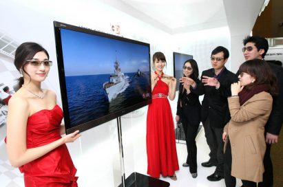 Another view of LG’s NEW CINEMA 3D TV with models standing next to it and people looking at it wearing 3D glasses