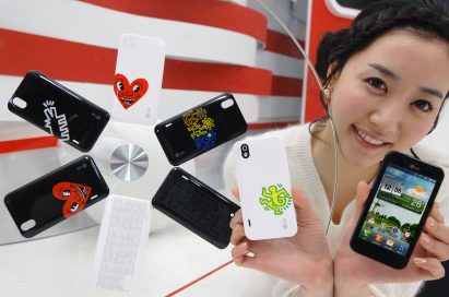 A model holds up two LG Optimus Black phones, showing off the front and rear of the device while next to 6 different back cover designs from the Keith Haring Foundation