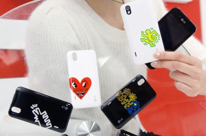 A model holds up two LG Optimus Black phones, showing off the front and rear of the device while next to 6 different back cover designs from the Keith Haring Foundation