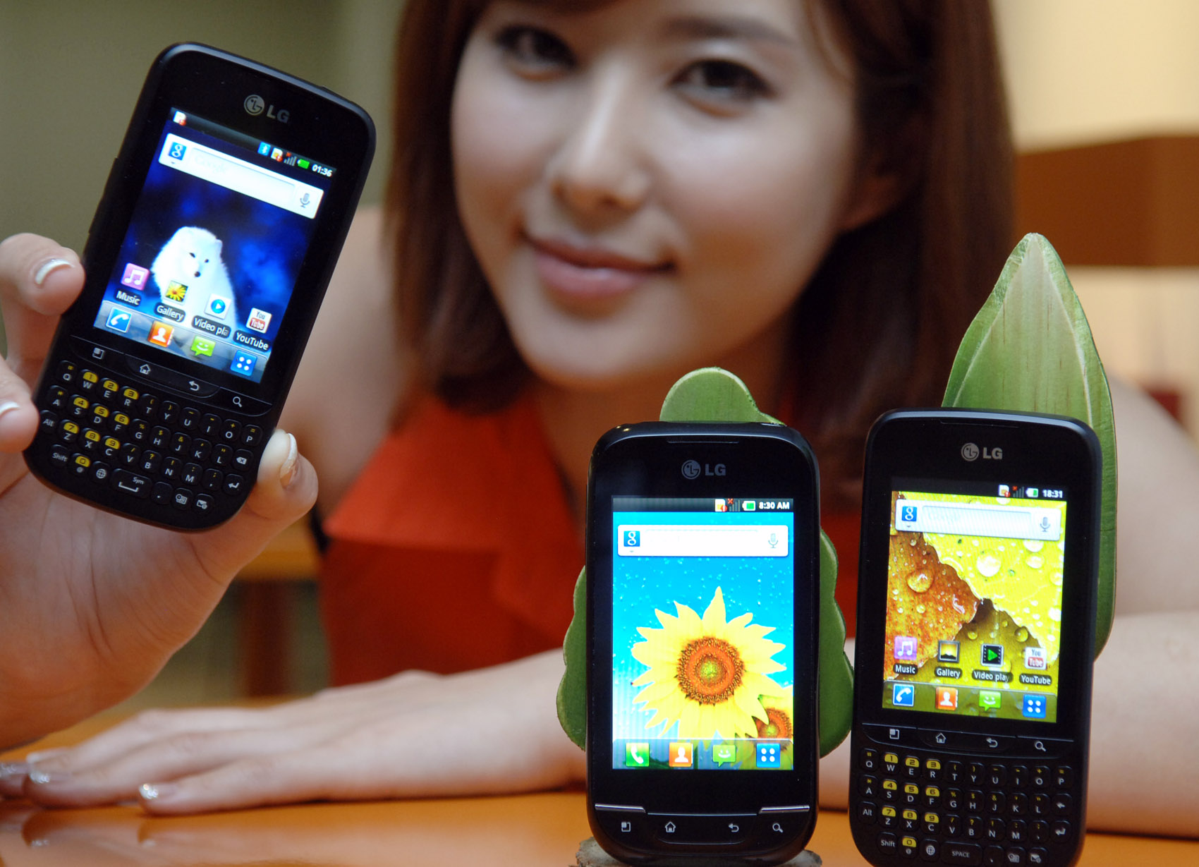 A model holds up LG Optimus Pro and shows its front view while LG Optimus Pro and LG Optimus Net are displayed in front of her