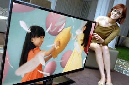 A female model wearing 3D glasses tries to touch the screen of LG's LW980S 3D LCD TV while the TV displays little girls playing a pillow fight.
