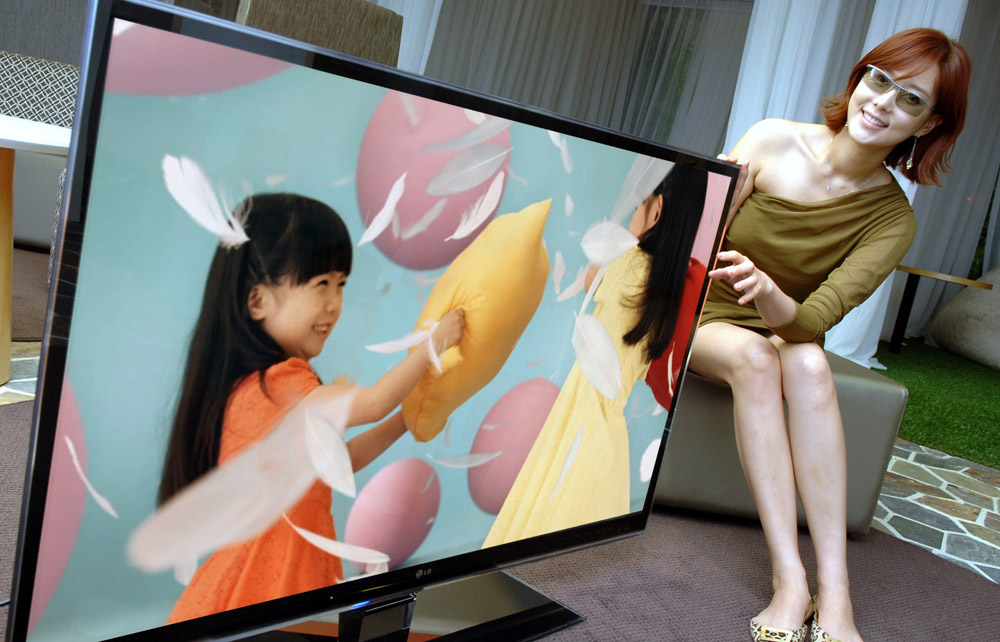 A female model wearing 3D glasses tries to touch the screen of LG's LW980S 3D LCD TV while the TV displays little girls playing a pillow fight.