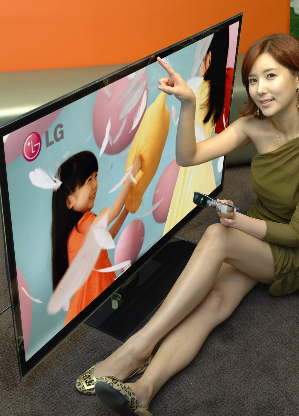 A female model points at the screen of LG's LW980S 3D LCD TV with 3D glasses in her hand.