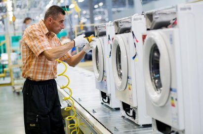 A male worker assembling the compartments of washing machines at an LG factory